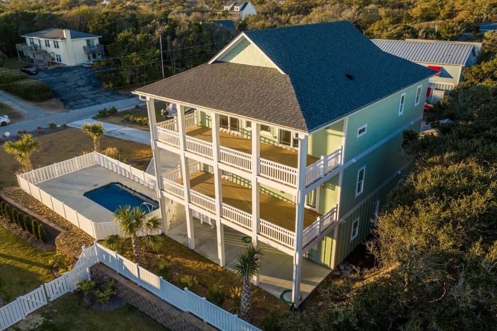 Arial photo of three-story mint green home with three decks with white railings.