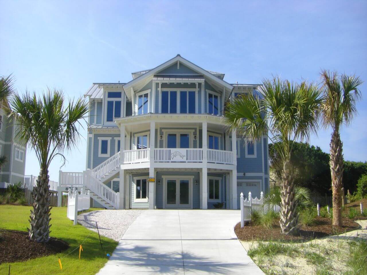 Front view of Colonial style house, blue, White picket fence, and palm trees.